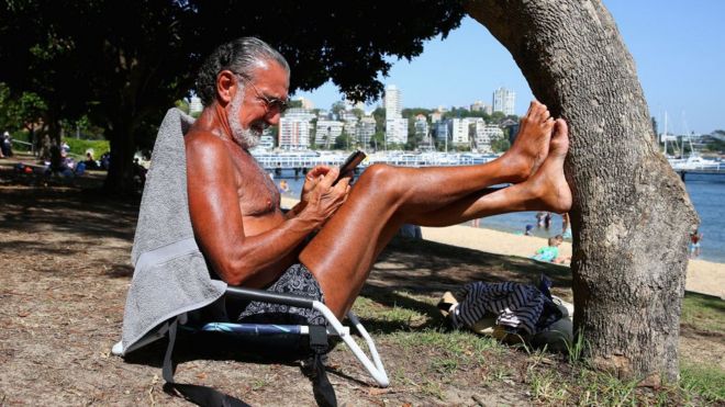 Пляжник читает свой телефон на солнце в Сиднее во вторник