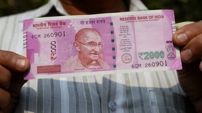 Индийский мужчина показывает новую банкноту в 2000 рупий после обмена своими старыми банкнотами в 500 и 1000 рупий в одном из банков Нью-Дели 10 ноября 2016 года