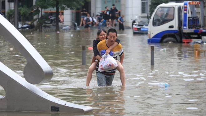 A man carrying a woman wades through a flooded road following heavy rainfall in Zhengzhou