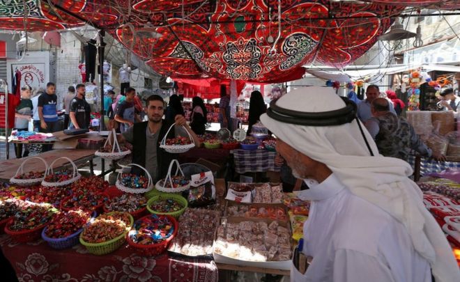 Продавец продает сладости, пока палестинцы делают покупки на рынке в преддверии предстоящего праздника Ид аль-Фитр, знаменующего конец мусульманского священного месяца Рамадан, в Рафахе в южной части сектора Газа 14 июня 2018 года