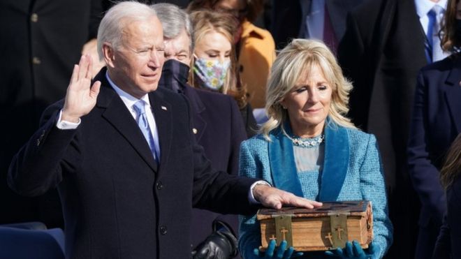 Joe Biden takes his oath with one had on the Bible