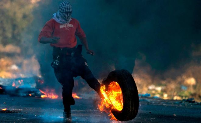 Палестинский протестующий пинает горящие шины в сторону израильских сил безопасности - 9 декабря 2017 года