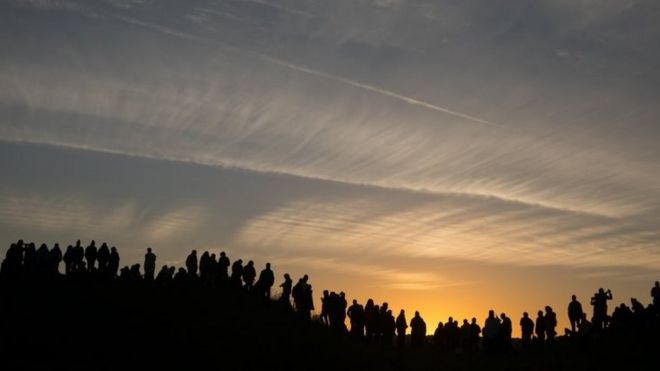 Люди стоят на холме и смотрят на восход солнца