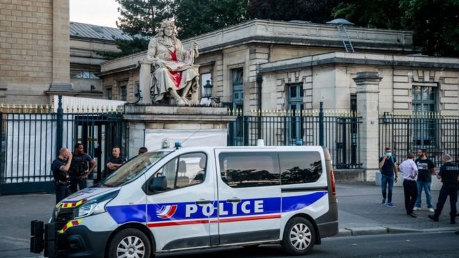 Authorities stand around the statue of Jean-Baptiste Colbert, vandalised by an activist