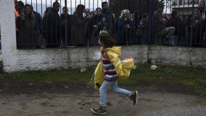 Девушка-беженка бежит, когда местные жители проводят акцию протеста возле школы в греческой деревне Профитис, примерно в 35 километрах (22 милях) к востоку от Салоник, в понедельник, 10 октября 2016 года. Жители закрыли один вход в школу и прикрепили к ней греческие флаги в знак протеста
