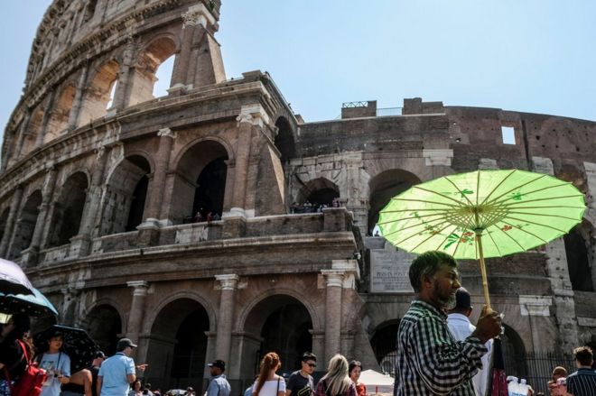 Мужчина держит зонтик, чтобы защитить себя от солнца во время летнего дня перед древним Колизеем в центре Рима