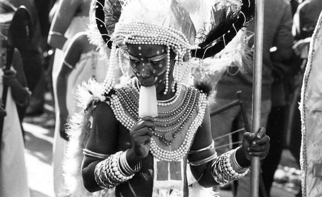 Участник карнавала сосет леденец во время парада в Ноттинг Хилл Карнавал в 1980 году
