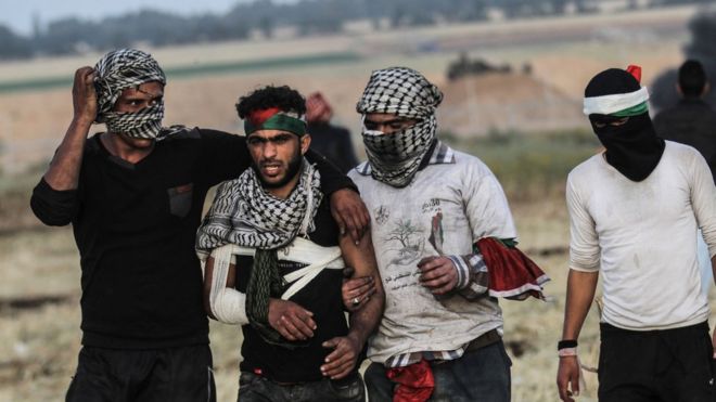 Палестинские демонстранты помогают раненому во время столкновений с израильскими силами возле границы с Израилем 2 апреля 2018 года