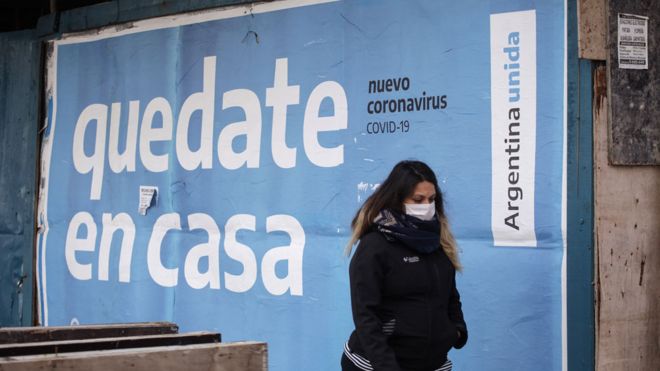 A young woman walks in Buenos Aires in front of an outdoor poster asking people to stay at home