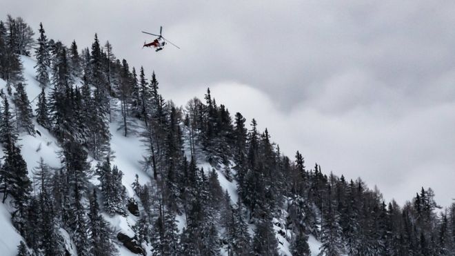 Спасательный вертолет покидает место схода лавин после того, как два человека были сметены в Швейцарии 18 февраля 2018 года.