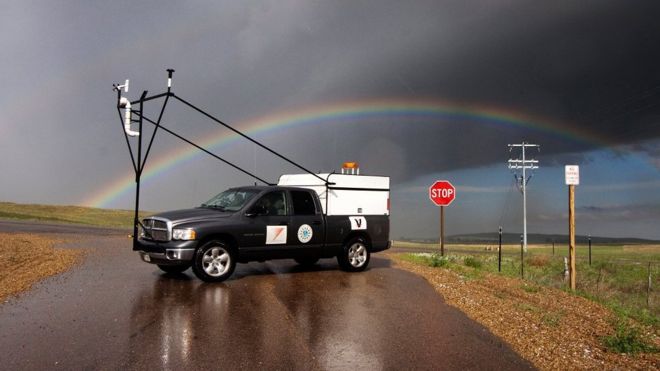 Imagem mostra veículo usado por pesquisadores para estudar as tempestades da Argentina, estacionado em um cenário com céu nublado e um arco-íris de fundo