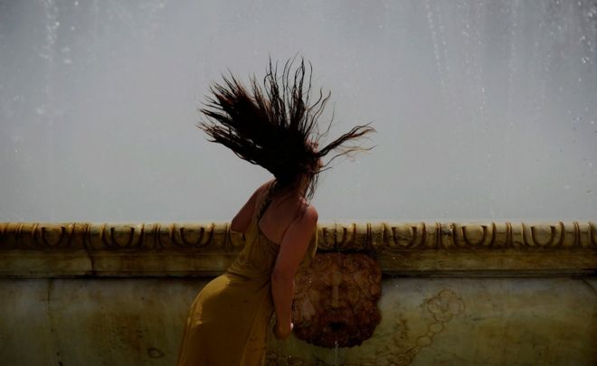 Женщина освежается в фонтане на площади Испании в жаркий летний день в Севилье