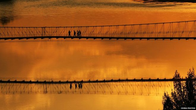 Туристы идут по висячему мосту над рекой Эртикс, чтобы полюбоваться закатом на мелководье Укай, или Красочным мелководьем, типичным примером рельефа лавы 13 сентября 2007 года в округе Буэрджин Синьцзян-Уйгурского автономного района, Китай.