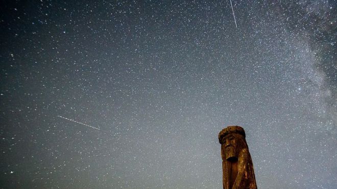 Estrelas cadentes cruzam o céu noturno sobre um ídolo de madeira perto da vila de Ptich, a cerca de 25 km de Minsk, durante o pico da chuva de meteoros Perseidas anual em 15 de agosto de 2015