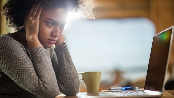 Mulher segura a cabeça enquanto olha angustiada para tela de computador