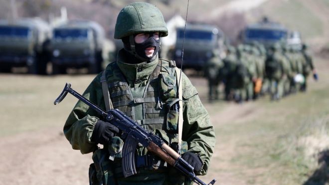Вооруженный человек, предположительно российский солдат, стоит на страже у военной базы в Перевальном