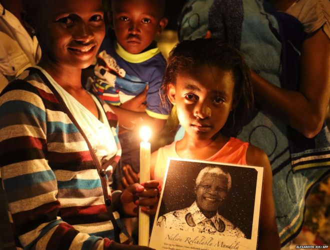 Люди позируют со свечой в память о бывшем президенте ЮАР Нельсоне Манделе возле его дома в Йоханнесбурге