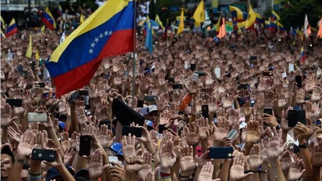 Люди поднимают руки во время массового митинга оппозиции против президента Николаса Мадуро, в ходе которого глава Национального собрания Венесуэлы Хуан Гуайдо (вне рамок) объявил себя «исполняющим обязанности президента» страны в годовщину восстания 1958 года, которое свергло военную диктатуру, в Каракас 23 января 2019 года