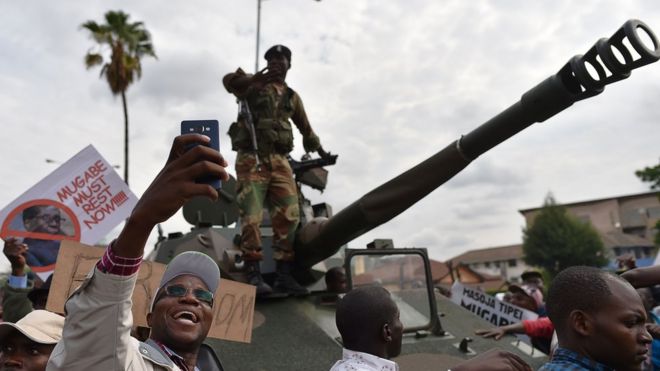 Мужчина делает селфи-снимок солдата Зимбабвийских сил обороны, стоящего на танке во время марша на улицах Хараре 18 ноября 2017 года, чтобы потребовать от 93-летнего президента Зимбабве уйти в отставку
