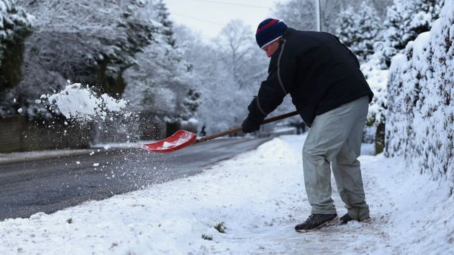 Мужчина сгребает снег в Бакстоне, Дербишир