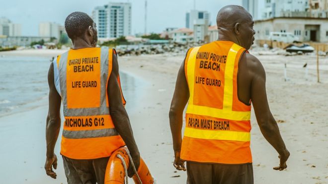 Два спасателя гуляют по пляжу в Лагосе, Нигерия