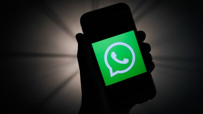La silueta ensombrecida de una mano y un móvil con el logo de WhatsApp