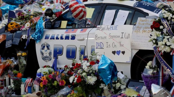 Примечания, цветы и другие предметы украшают полицейскую машину у временного мемориала перед полицейским управлением Далласа 9 июля