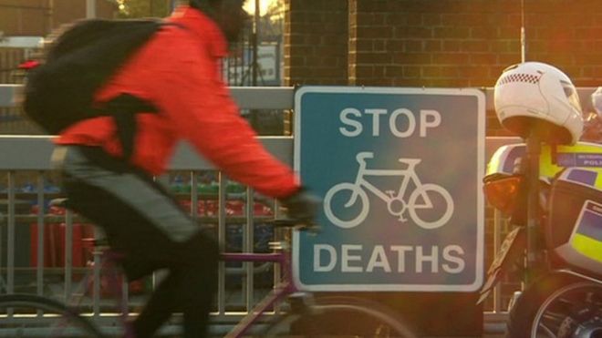 Человек ездит на велосипеде мимо знака, говорящего: Остановите смертельные случаи цикла