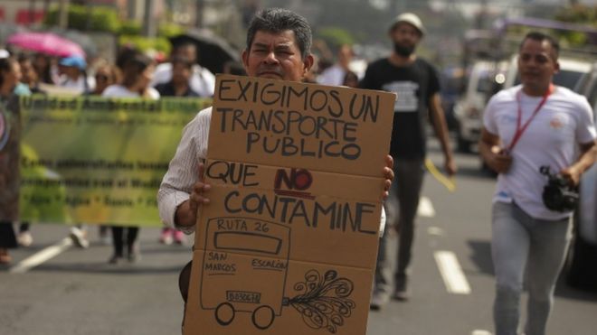 Un hombre sostiene un cartel demandando "transporte público que no contamine". en San Salvador.