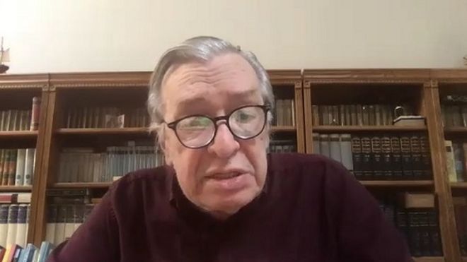 Olavo de Carvalho dá entrevista em frente a computador, com estante de livros atrás