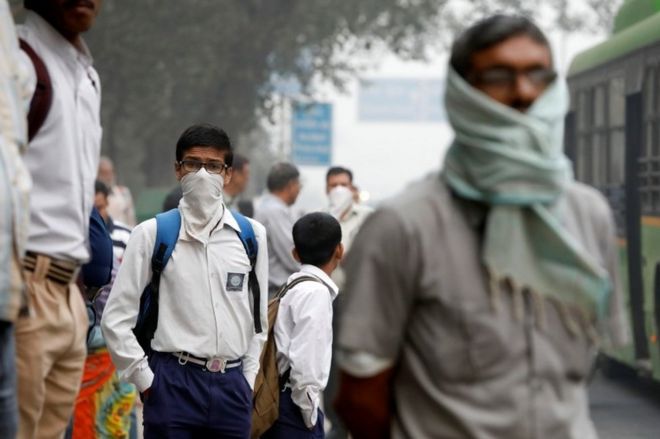 Школьник закрывает лицо платком, ожидая пассажирского автобуса темным утром в Нью-Дели, Индия, 8 ноября 2017 г.