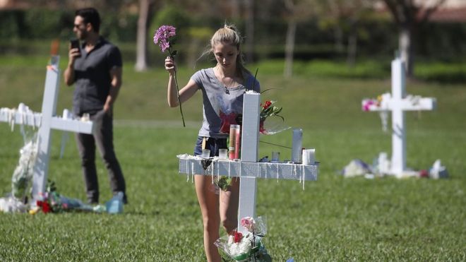 Молодая женщина возлагает цветы к мемориалу, где чествуют жертв массовой стрельбы в средней школе имени Марджори Стоунман Дуглас, в Пайн-Трейл-Парк 16 февраля 2018 года в Паркленде, Флорида