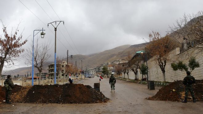 Сирийские проправительственные силы стоят у входа в осажденный повстанческий город Мадайя на баррикаде, установленной у входа, в ожидании колонны помощи от Сирийского Арабского Красного Полумесяца 14 января