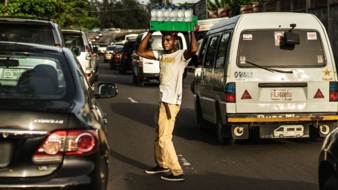 Мужчина продает воду посреди оживленной дороги в Лагосе