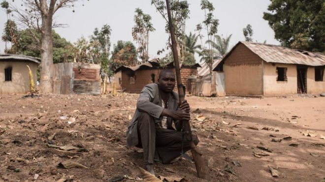 Бдительный ополченец сидит на земле с пистолетом в деревне Бакин Коги в штате Кадуна на северо-западе Нигерии, который недавно подвергся нападению со стороны подозреваемых пастухов фулани