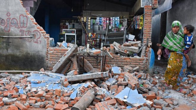 A woman walks past debris from a collapsed wall following a strong earthquake in Lendang Bajur Hamlet, Lombok island,