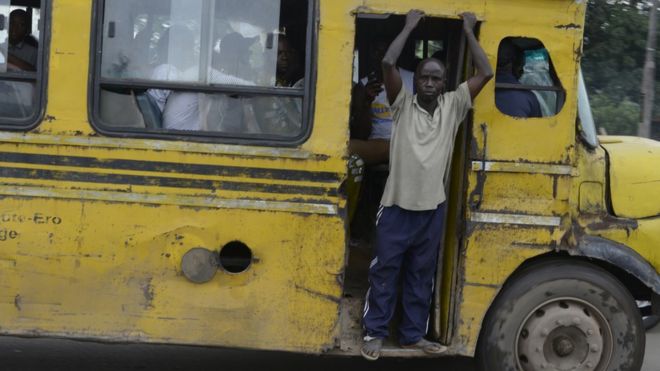 Человек смотрит в открытую дверь желтого автобуса в Лагосе, Нигерия