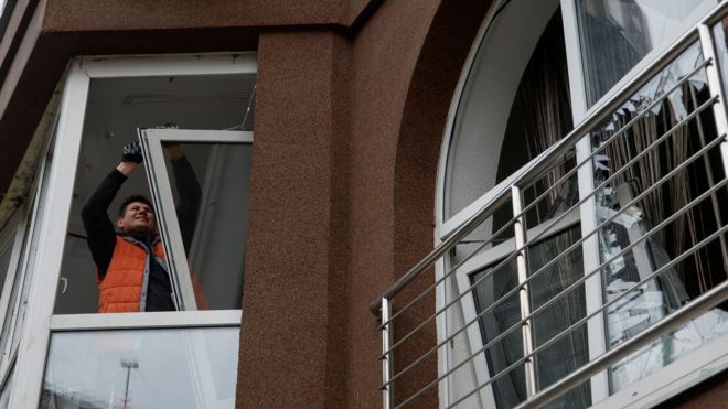 Man dismounting window of residential building damaged by Russian drone