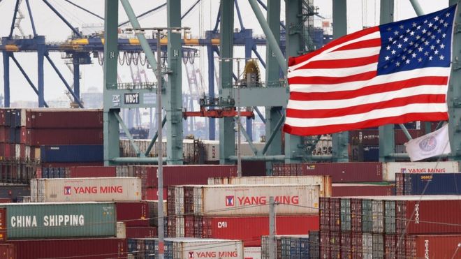 Китайские морские контейнеры хранятся рядом с флагом США после того, как они были выгружены в порту Лос-Анджелеса в Лонг-Бич, штат Калифорния, 14 мая 2019 года.
