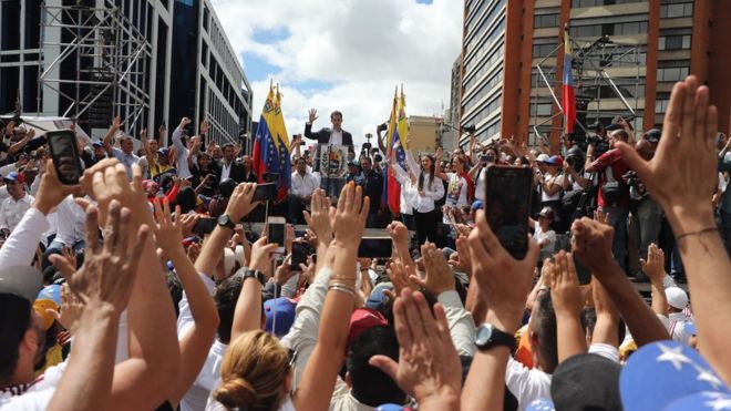 Граждане поднимают руки, когда Хуан Гуайдо, председатель парламента Венесуэлы, объявляет о том, что он принимает исполнительные полномочия