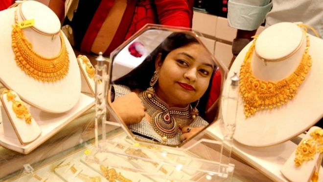 தீபாவளி கொண்டாட்டங்கள் பல நாட்கள் தொடர்வன. அதில் ஒரு நாளான தன்தேரஸ் தினத்தன்று நகைக்கடையில் நகை வாங்க சென்று புன்னகையுடன் நகையணிந்து அழகு பார்க்கும் பெண்.