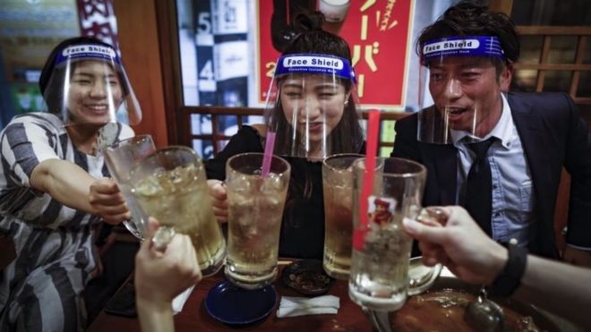 Клиенты носят пластиковые защитные маски для лица во время тостов в очках в Осаке, Япония