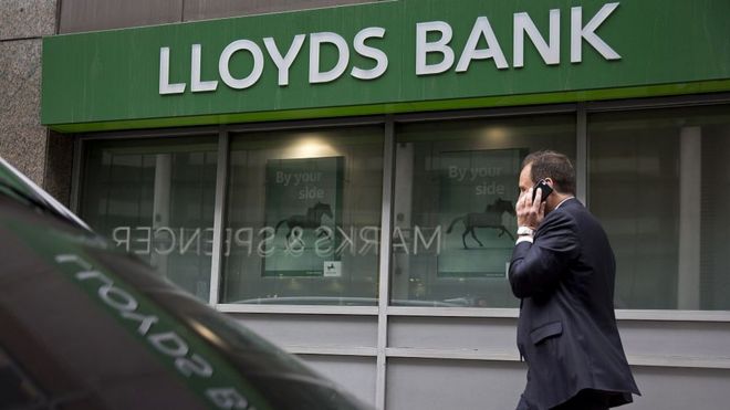 Человек по телефону проходит мимо отделения банка Lloyds