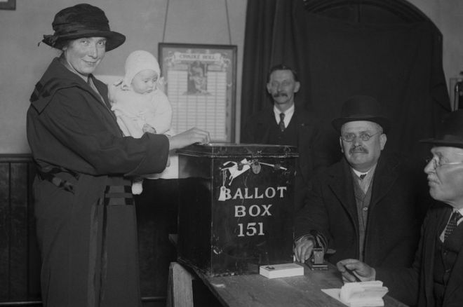Мать размещает голосование в урне в Южном Далвиче, держа ребенка на руках