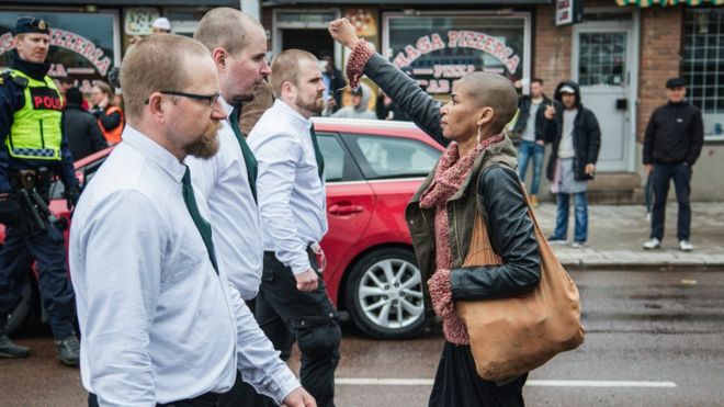 Одинокая женщина стоит с поднятым кулаком напротив демонстрантов в форме на воскресной нацистской демонстрации в Бурленге, Швеция