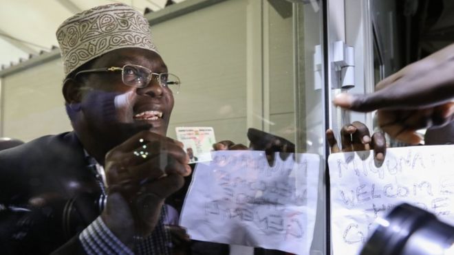 Mr Miguna holds his identification up to glass after being detained earlier this week in airport