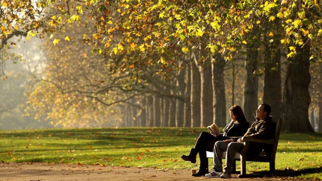 Dos personas sentadas en un banco en Hyde Park, en Londres, junto a una avenida de árboles