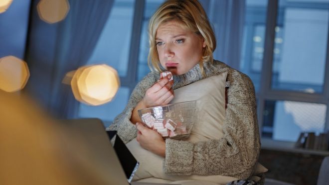 Mujer triste comiendo dulces frente a la computadora.