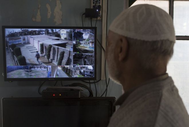 Пожилой мужчина наблюдает за монитором камер видеонаблюдения у себя дома