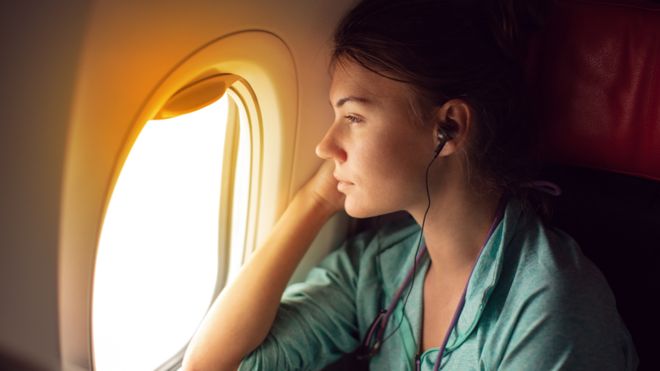 Mulher sentada dentro de um avião, olhando pela janela com fones de ouvido